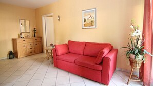 A living room with a red sofa, a wooden cabinet, a small table, and a potted plant.