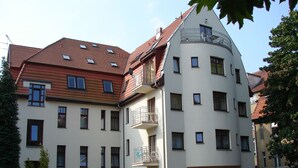 A multi-story residential building with balconies, a car parked in front, and a well-maintained lawn.
