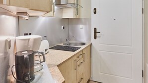 A compact kitchen with wooden cabinets, a white door, and a stainless steel range hood. - Apartamenty Swinoujscie - Bursztyn (Swinoujscie)