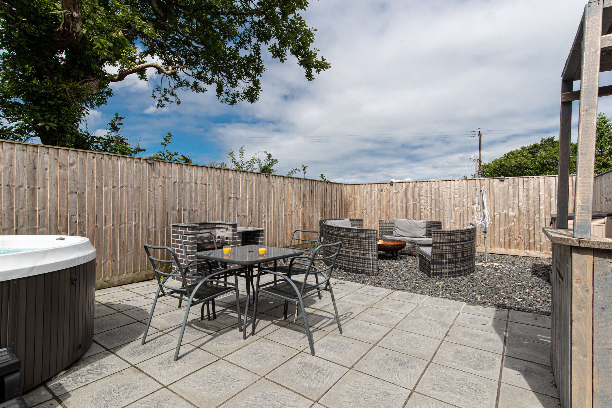 Een terras buiten met een hottub, eettafel en stoelen.
