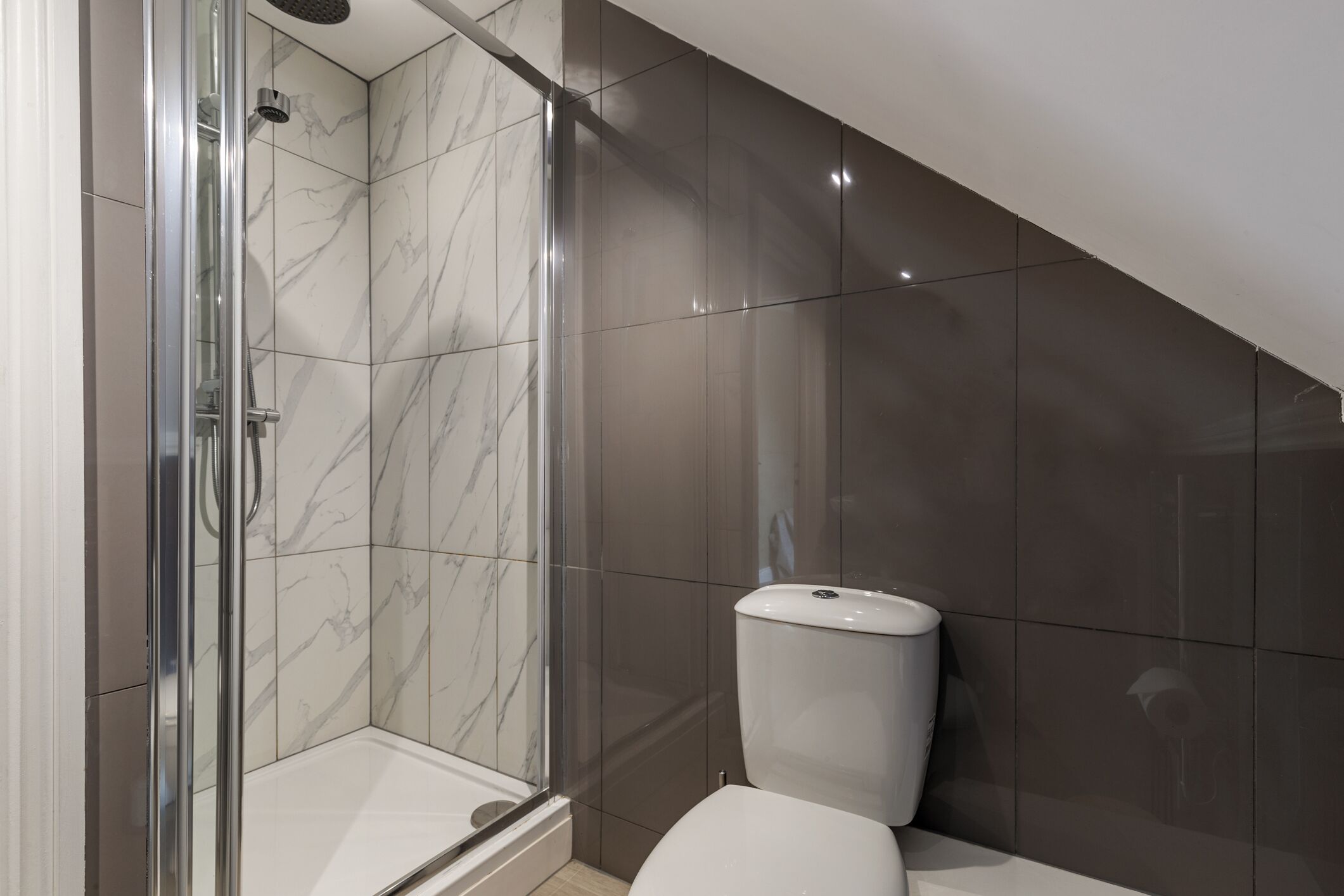 Een moderne badkamer met een douchecabine van glas, een wit toilet en wanden met een marmerlook.