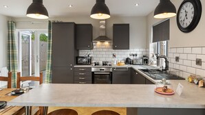 Une cuisine moderne avec des meubles de couleur sombre, un îlot central et des luminaires suspendus.
