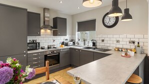 Une cuisine moderne avec des meubles gris, un îlot central, un four à micro-ondes, une cuisinière et un évier. Il y a une horloge au mur et un vase de fleurs sur le plan de travail.