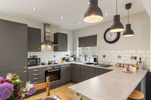 A modern kitchen with grey cabinets, a central island, a microwave, a stove, and a sink. There is a clock on the wall and a vase of flowers on the counter.