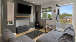 Un salon moderne doté d’un téléviseur à écran plat, d’une cheminée, de canapés gris et offrant une vue sur l’extérieur.