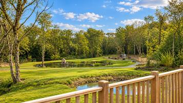 A golf course with a wooden deck in the foreground, surrounded by lush greenery and trees.
