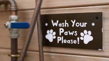 A sign that reads "Wash Your Paws Please!" with paw prints, attached to a wooden wall near a hose.