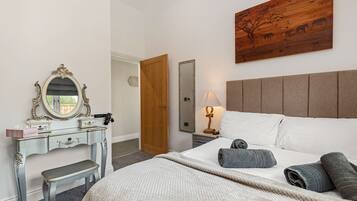 Een slaapkamer met een bed, een kaptafel met spiegel, een houten hoofdeinde en een kunstwerk aan de muur.