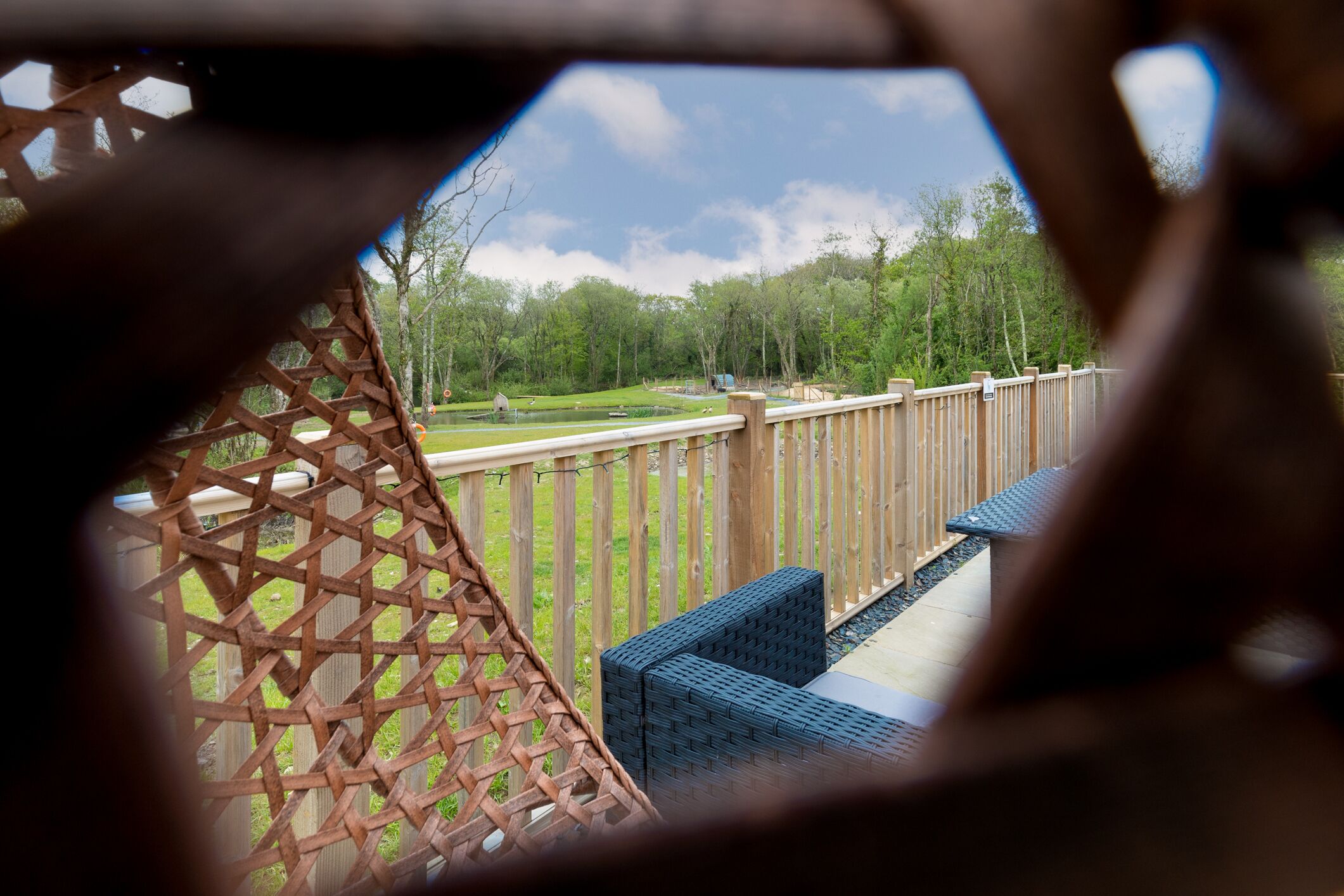 Una terraza de madera con valla celosíaca, mobiliario exterior y vistas a un parque.