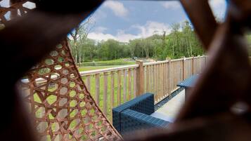 Una terraza de madera con valla celosíaca, mobiliario exterior y vistas a un parque.