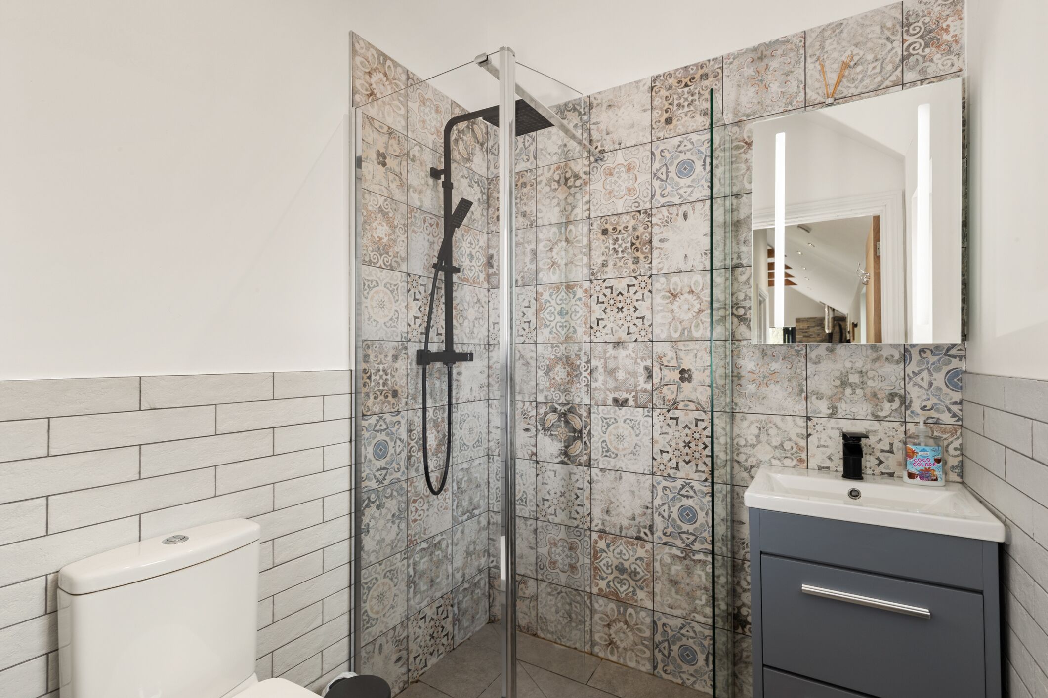 A bathroom with a shower, a toilet, a sink, and a mirror.