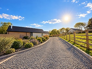 A gravel driveway leading to a house with a wooden fence on one side and a metal fence on the other. - Elm Tree Cottage (Tenby)