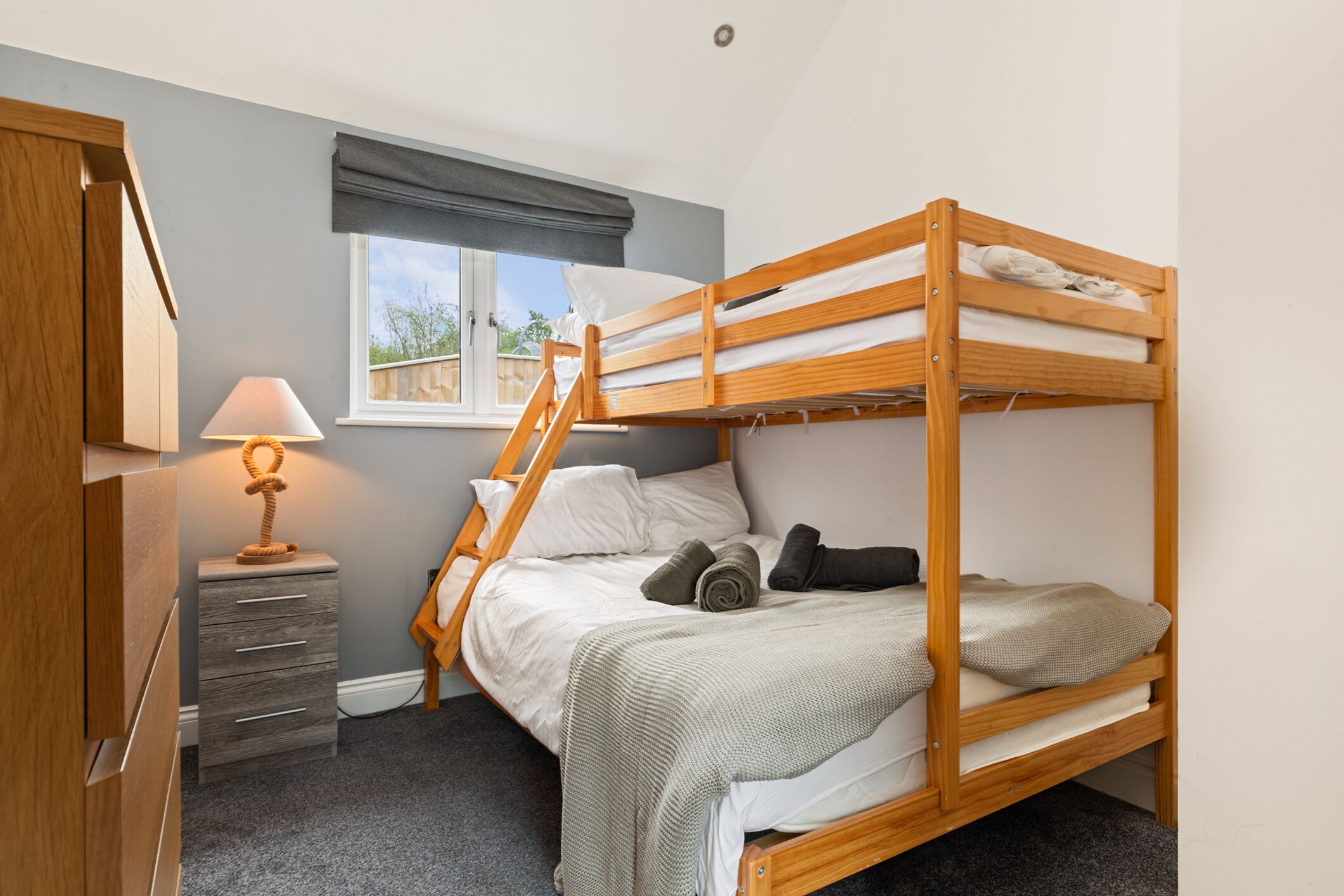 A bunk bed with a desk and lamp, grey walls, and a window with a view.
