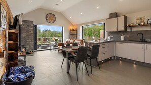 A modern kitchen with a dining area, a fireplace, and large windows offering a view of the outdoors. - Cedar Cottage (Tenby)