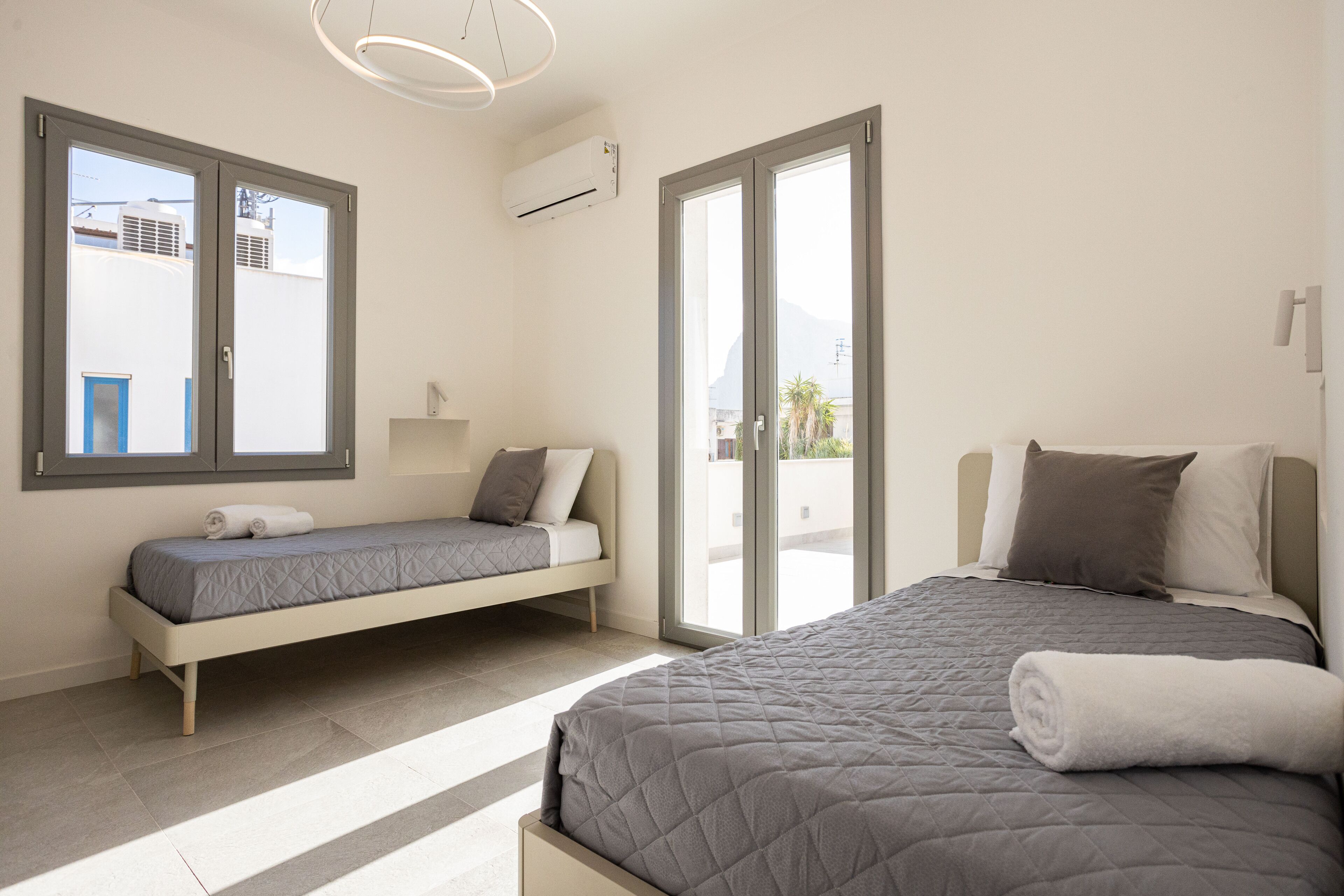 A modern bedroom with a large bed, a smaller sofa bed, and a sliding glass door leading to a balcony.