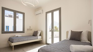 Una camera da letto moderna con un letto grande, un divano letto più piccolo e una porta scorrevole in vetro che dà su un balcone.