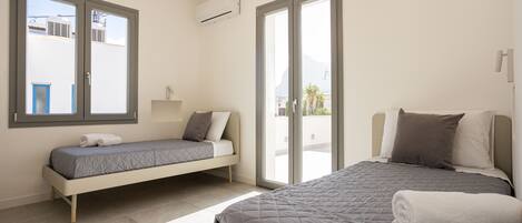 A modern bedroom with a large bed, a smaller sofa bed, and a sliding glass door leading to a balcony.