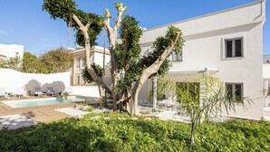 Una moderna casa a due piani con piscina, immersa nel verde e circondata da pareti bianche.