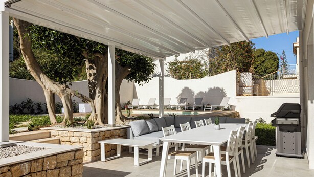 Patio esterno con tavolo da pranzo, sedie, barbecue e area piscina.