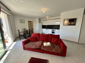 A modern living room with a red sofa, a dining area, and a kitchen.