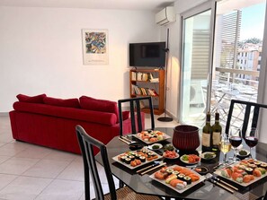 A dining area with a table set for sushi, a red sofa, a bookshelf, and a TV in a modern apartment.