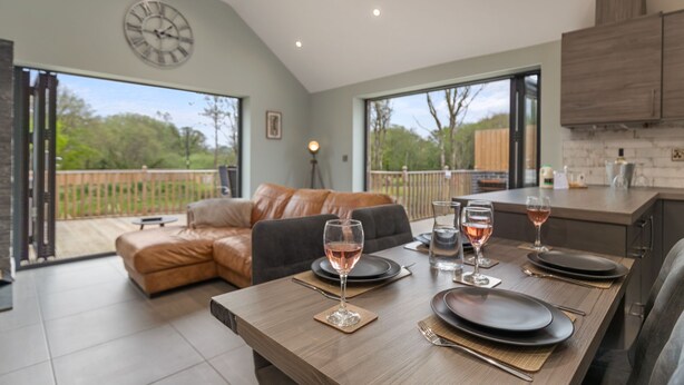 A dining area with a table set for four, a clock on the wall, and a view of the outdoors. - Fig Tree Cottage (Tenby)