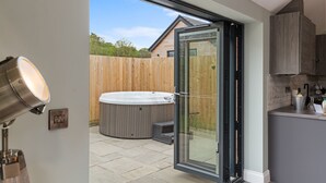 A modern kitchen with a built-in oven, a wooden fence, and a hot tub in the backyard. - Fig Tree Cottage (Tenby)
