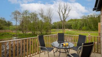 A wooden deck with a round table and four chairs, overlooking a grassy area with trees and a body of water.