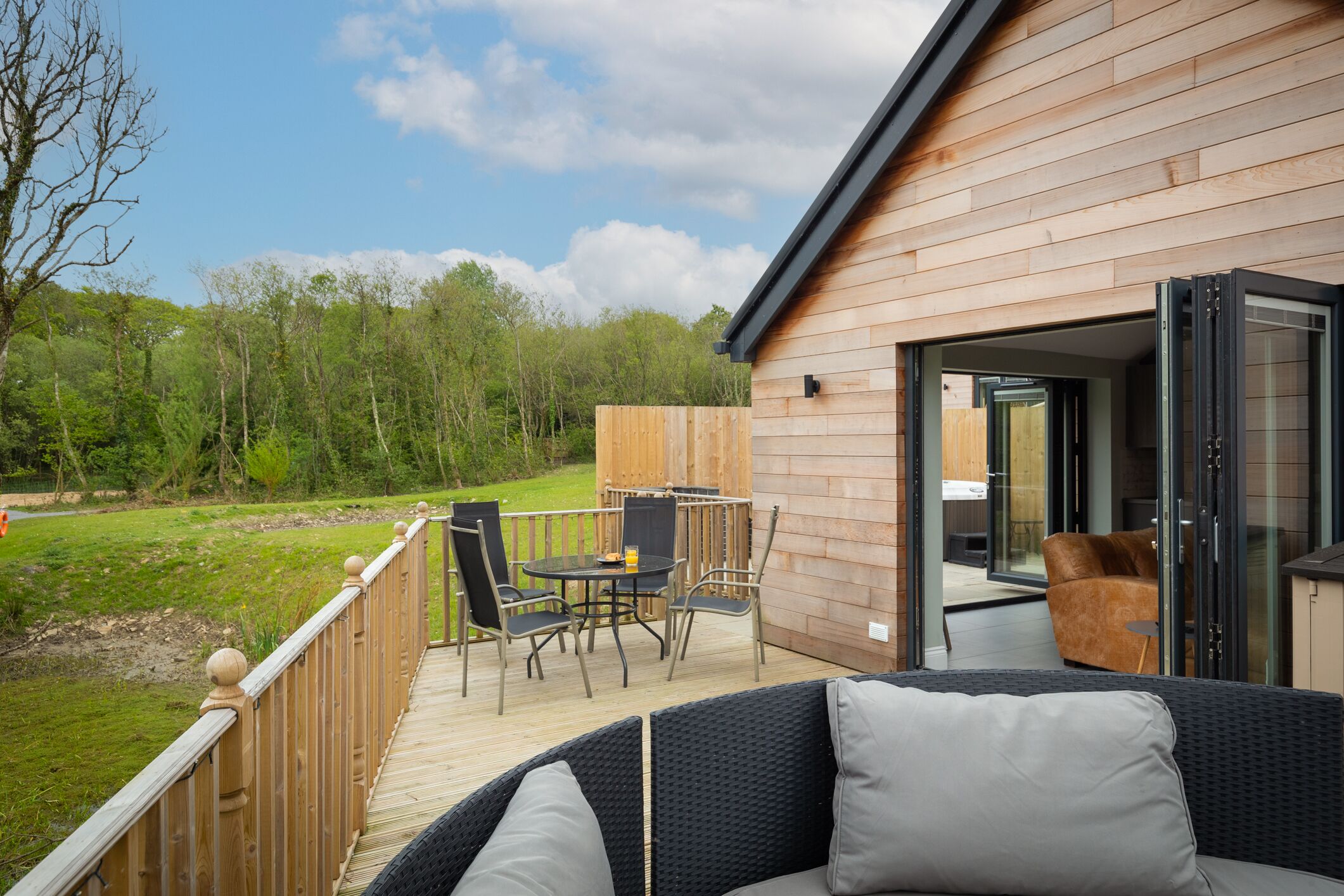 A wooden deck with outdoor furniture, a glass door leading inside, and a view of a green landscape.