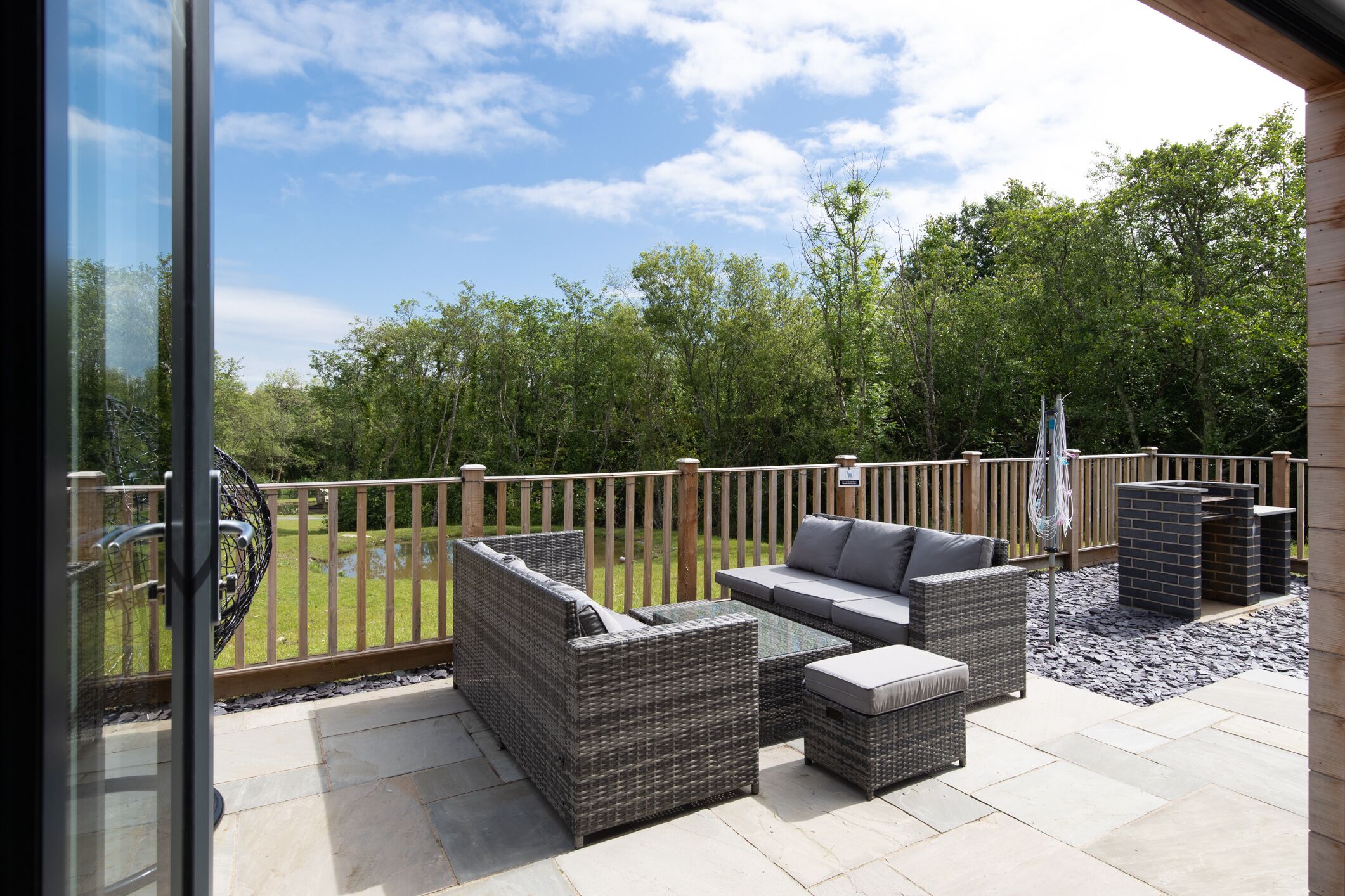 An outdoor patio with wicker furniture, a wooden fence, and a view of trees.