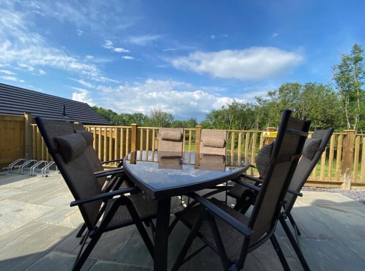 A patio with a table and four chairs, surrounded by a wooden fence and trees.