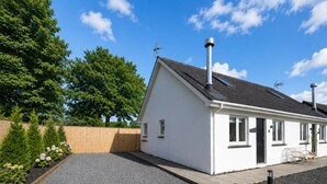 A single-story house with a sloped roof, a chimney, and a fenced garden area with various plants.