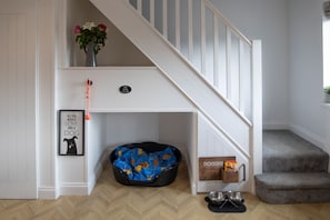 A pet-friendly room with a dog bed, a dog bowl, and a staircase. - Hazel Cottage (Tenby)