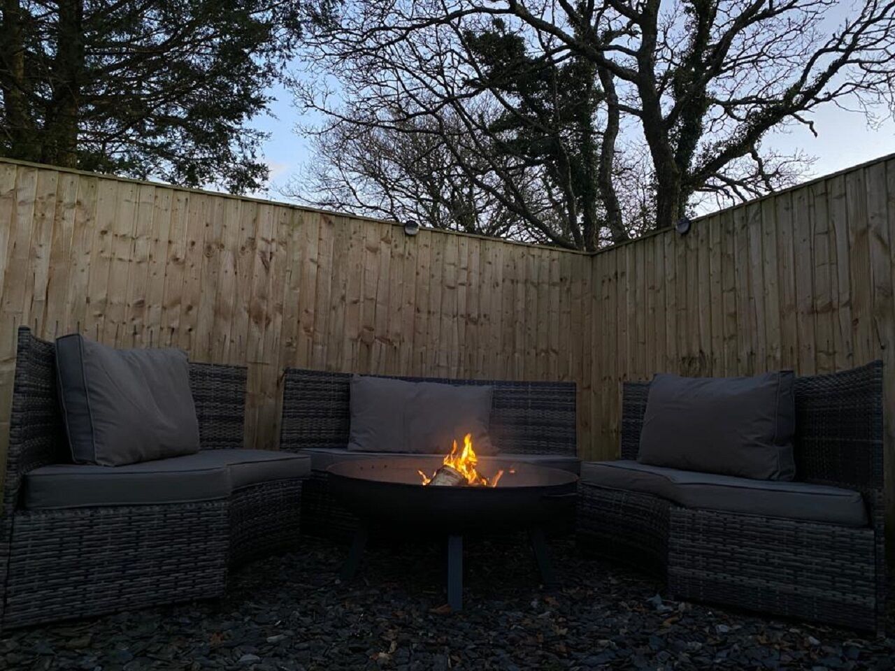 An outdoor seating area with a fire pit in the center, surrounded by wicker furniture.