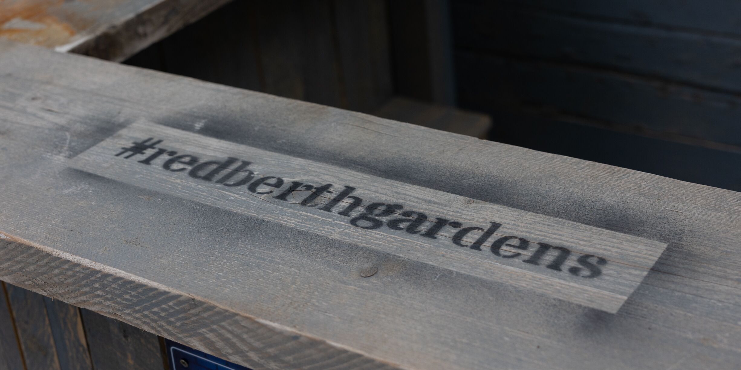 A wooden sign with the hashtag #redberthgardens.