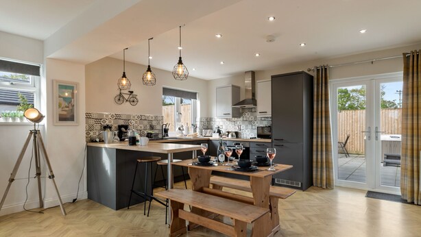 A modern kitchen with wooden benches, pendant lights, and a herringbone floor pattern.