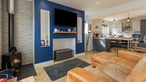 A modern living room with a fireplace, a television, and a kitchen area with bar stools.