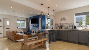 A modern kitchen with a wooden dining table, bar stools, and pendant lights.