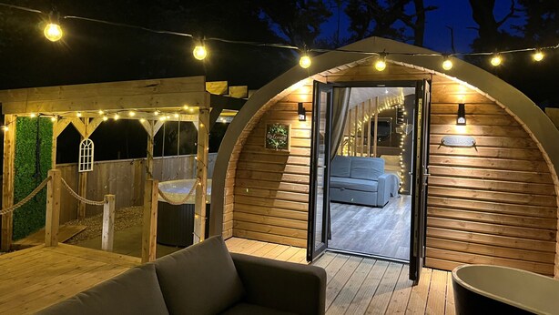 A cozy, semi-open wooden structure with a sofa and a bathtub, illuminated by string lights. - Calon (Tenby)