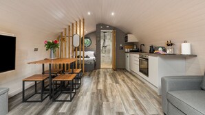A compact, modern kitchen with wooden flooring, a dining area with benches, and a grey sofa. - Calon (Tenby)