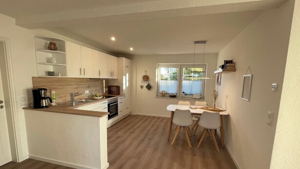 Een moderne keuken met een centraal eiland, witte keukenkastjes en een eethoek met tafel en stoelen.