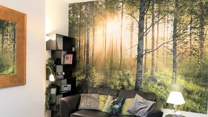A living room with a forest mural, a black leather sofa, a side table with a lamp, and a bookshelf. - Central Wigan Welcoming Townhouse Sleeps up to 6 (Wigan)