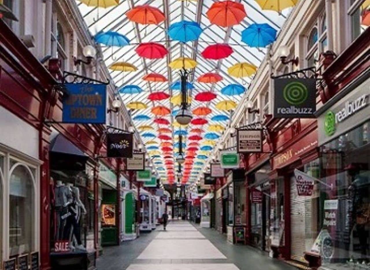Un pasillo comercial cubierto con sombrillas de colores y diversas tiendas.