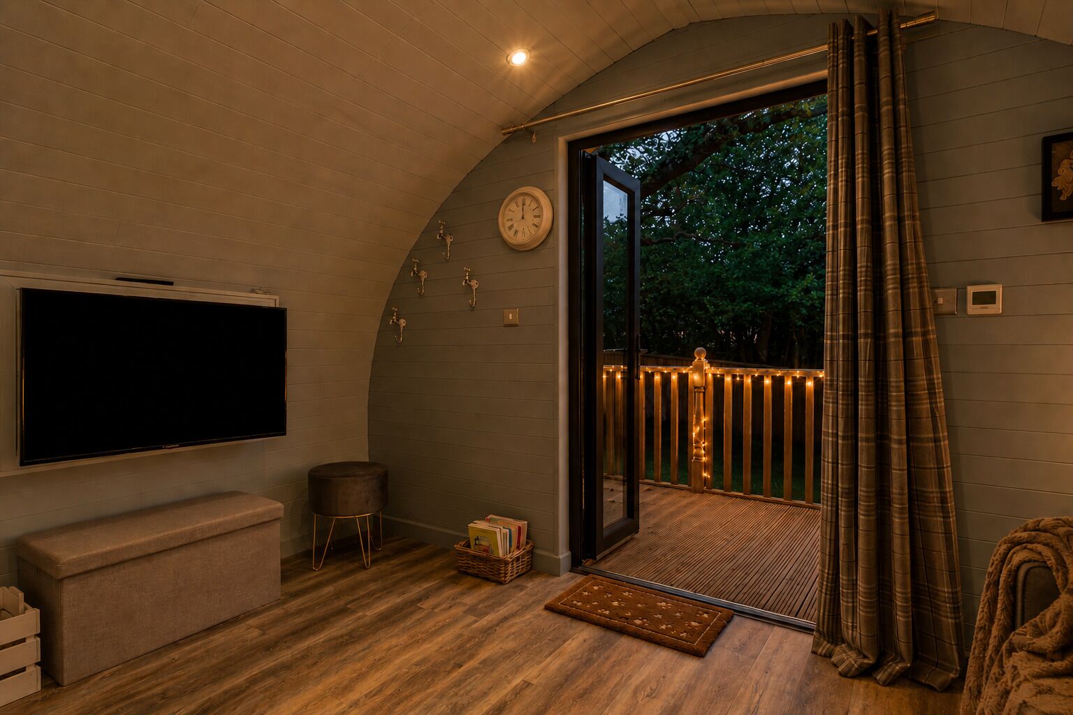 A cozy room with a flat-screen TV, a cushioned bench, a small stool, and a wooden floor.