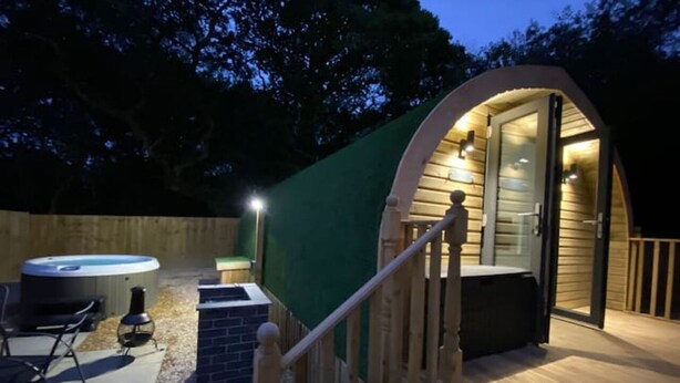 A cozy outdoor hot tub area with a wooden deck, a hot tub, and a seating area. - Cwtch (Tenby)