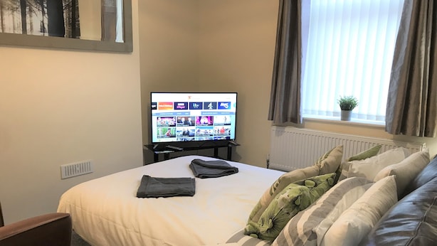 Une chambre d’hôtel avec un lit, un téléviseur affichant une liste des chaînes, une fenêtre avec des rideaux et une plante sur le rebord de la fenêtre.