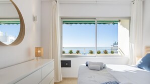 A hotel room with a bed, a window with a view of the sea, a bedside table, and a mirror. - Bright Apartment with Front Sea Views (Marbella)