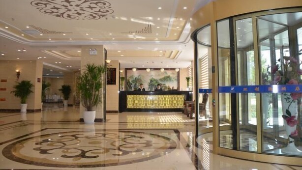 Een hotel lobby met een receptiebalie, potplanten en een glazen lift.