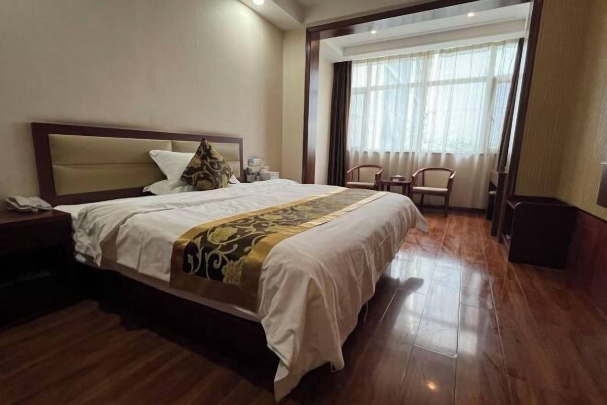 Une chambre d’hôtel avec un grand lit, un plancher en bois, une table de chevet, une chaise et une fenêtre avec des rideaux.