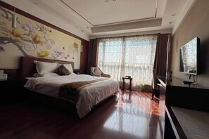 Ein Hotelzimmer mit einem großen Bett, einem Fernseher, einem Schreibtisch und einem Fenster mit Vorhängen.
